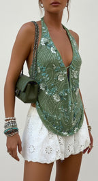 Woman wearing a whimsical, beaded green halter neck top and white shorts with a green handbag.