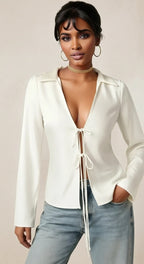 Woman wearing a white blouse with a deep neckline and light blue jeans on a beige background