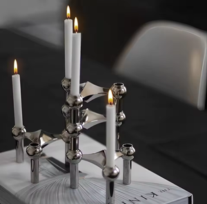 A stainless steel stackable molecular taper candle holder with three lit candles on a table, showcasing the sleek design and metallic finish.