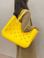A person carrying a yellow EVA plastic tote bag with a solid pattern and circular holes on the sides.