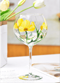 A hand-painted crystal red wine glass with a yellow floral design, displayed on a table.