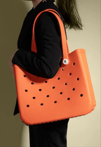 A person holding an orange EVA beach tote bag with a solid pattern and holes across the surface.
