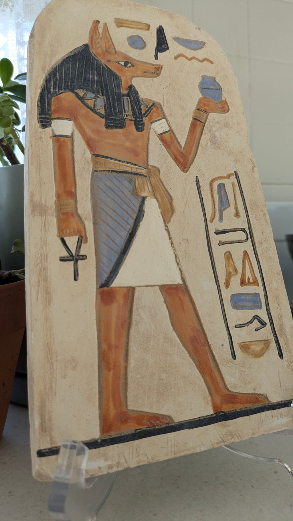 Decorative piece with an Egyptian-style figure and hieroglyphics on a stone plain background