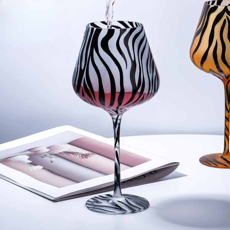 Zebra-striped wine glass being filled with red wine on a light gray background