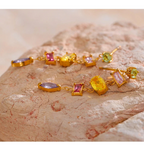 Gold bracelet with colorful gemstones on a stone surface, branded as Vogue.