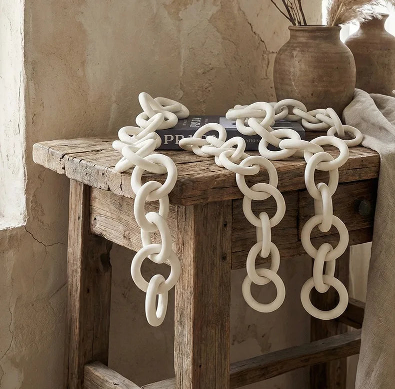 Decorative white chain on a rustic wooden table with a textured wall background