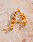 Gold earrings with small pastel gemstones on a beige stone surface