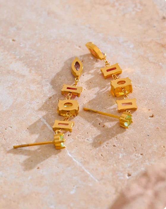 Gold earrings with small pastel gemstones on a beige stone surface