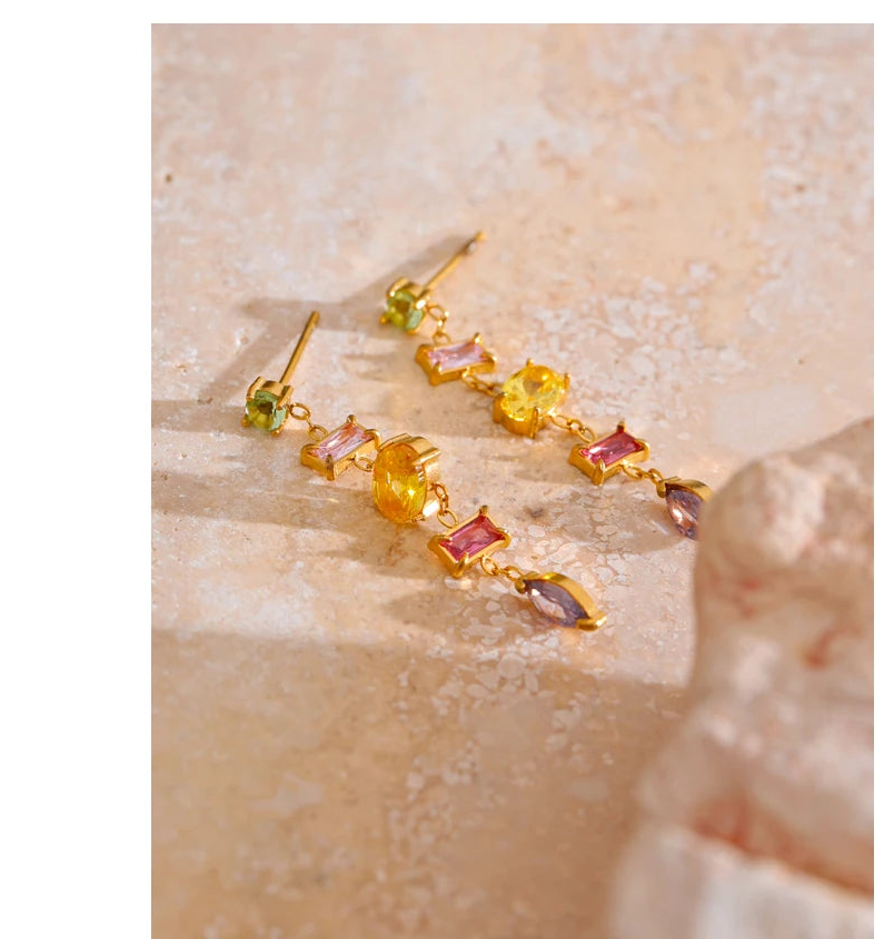 Gold earrings with colorful stones on a textured beige background