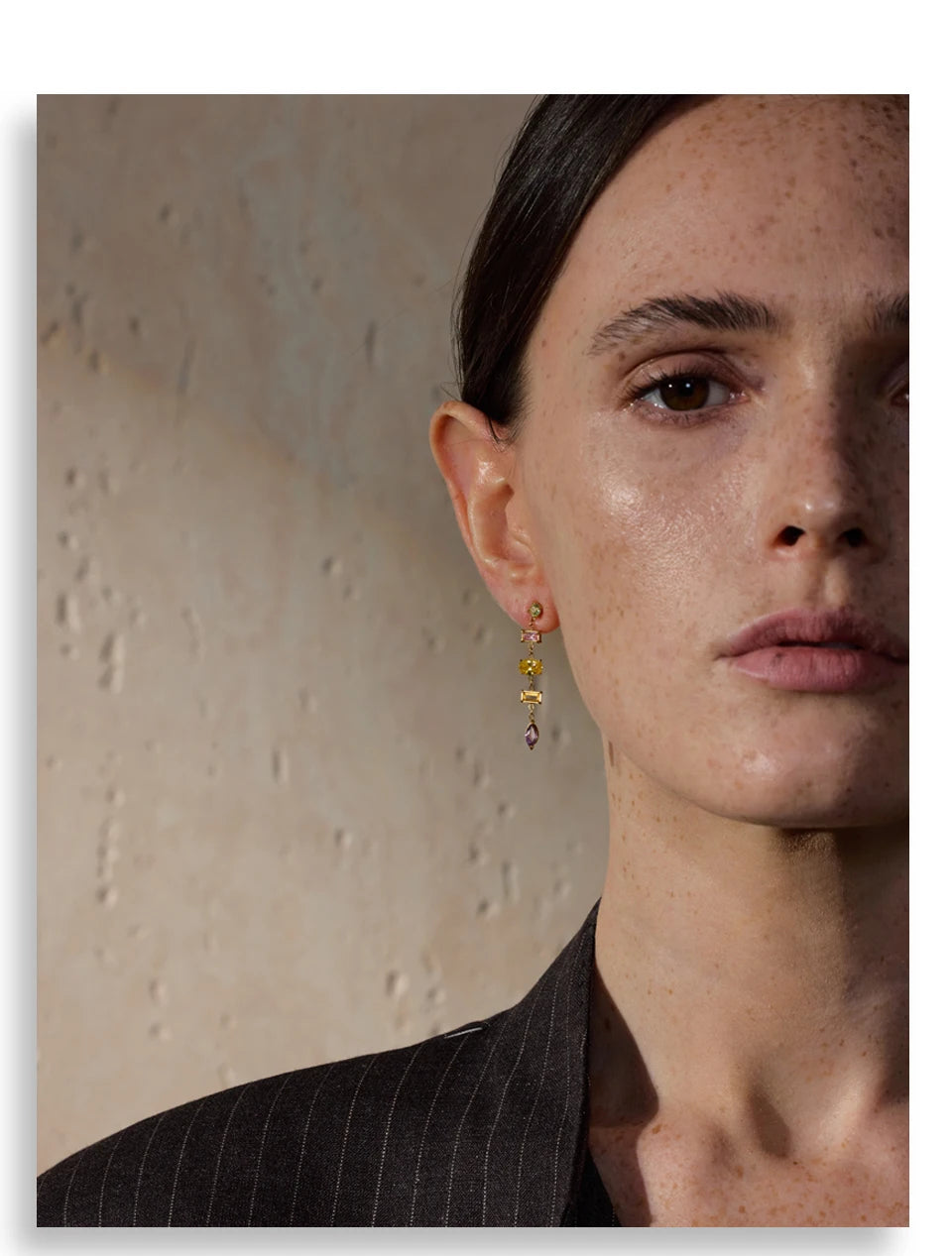 Close-up of a woman wearing pastel drop earrings with a neutral background