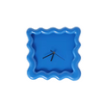 A square-shaped wall clock with a textured wave design and a cobalt blue color.