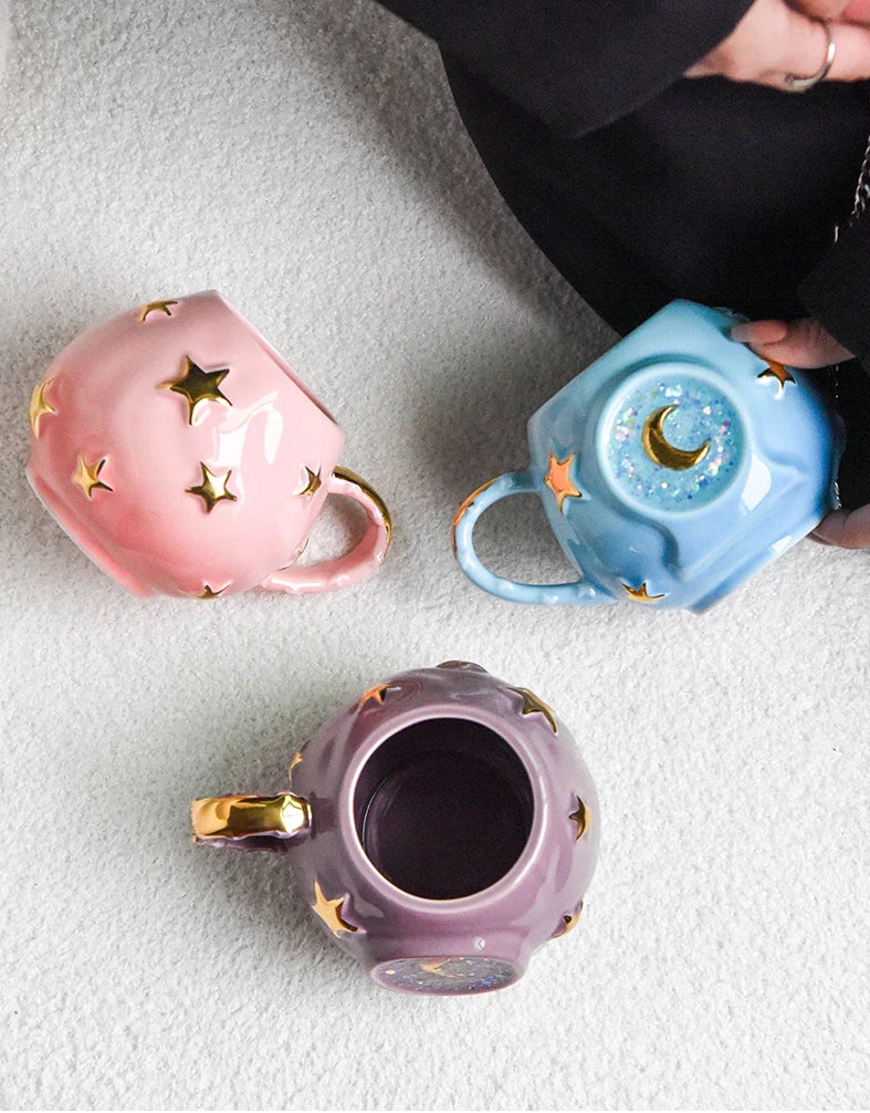 Three ceramic mugs with star and moon designs on a textured surface.