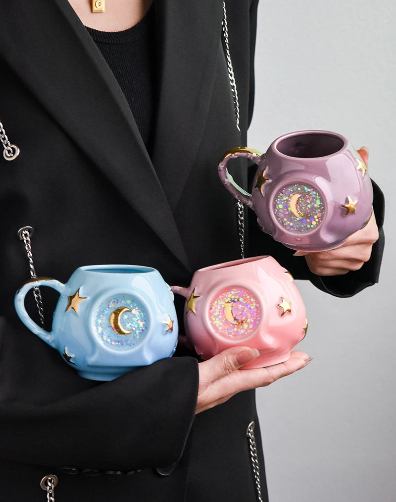 Person holding three decorative mugs with star and moon designs.