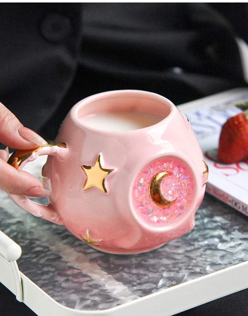 Pink mug with star and moon designs being held over a cup of coffee on a marble surface.
