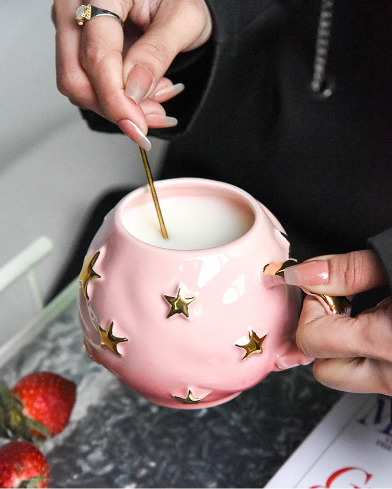 Person using a pink ceramic mug with star designs, holding a small object over it.